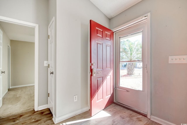 foyer entrance featuring light wood-type flooring, vaulted ceiling, and a textured ceiling