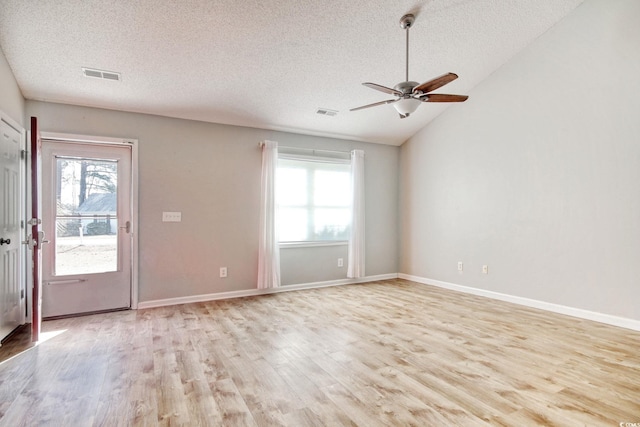 empty room with vaulted ceiling, plenty of natural light, a textured ceiling, and light hardwood / wood-style flooring