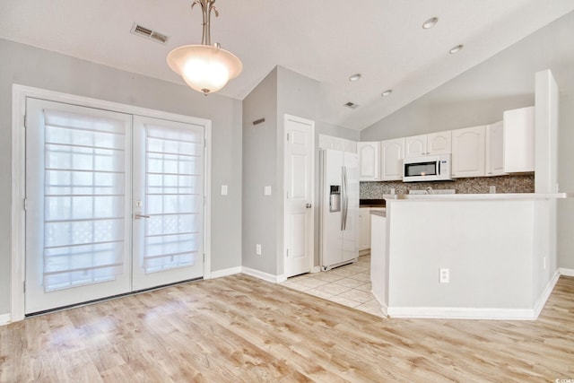 kitchen with lofted ceiling, refrigerator with ice dispenser, decorative light fixtures, white cabinetry, and tasteful backsplash