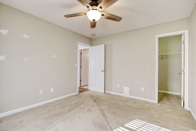 unfurnished bedroom with a spacious closet, ceiling fan, a closet, and light colored carpet