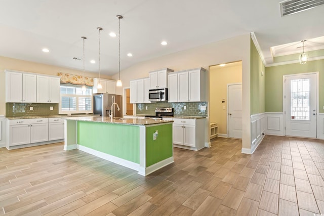 kitchen with a center island with sink, white cabinetry, hanging light fixtures, and stainless steel appliances