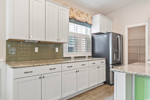 kitchen featuring white cabinetry, light stone countertops, stainless steel refrigerator with ice dispenser, and tasteful backsplash