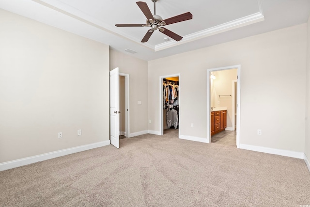 unfurnished bedroom featuring ceiling fan, a raised ceiling, ensuite bath, a walk in closet, and a closet