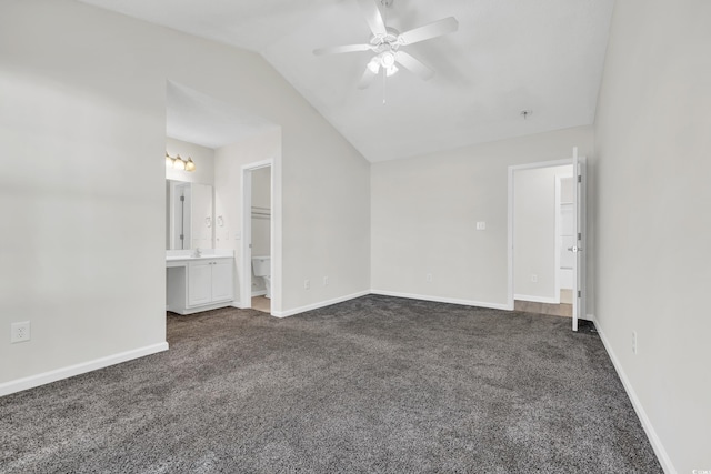 unfurnished bedroom featuring vaulted ceiling, ceiling fan, dark colored carpet, and ensuite bath