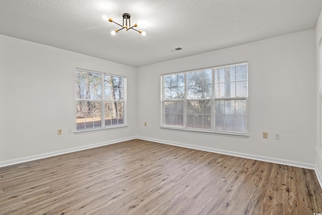 spare room featuring a textured ceiling, a chandelier, and light hardwood / wood-style flooring