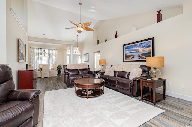 living room with ceiling fan with notable chandelier, wood-type flooring, and high vaulted ceiling