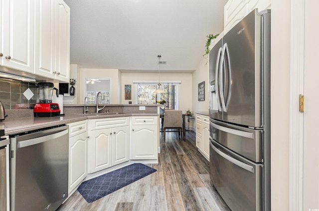 kitchen with kitchen peninsula, sink, hanging light fixtures, stainless steel appliances, and white cabinets