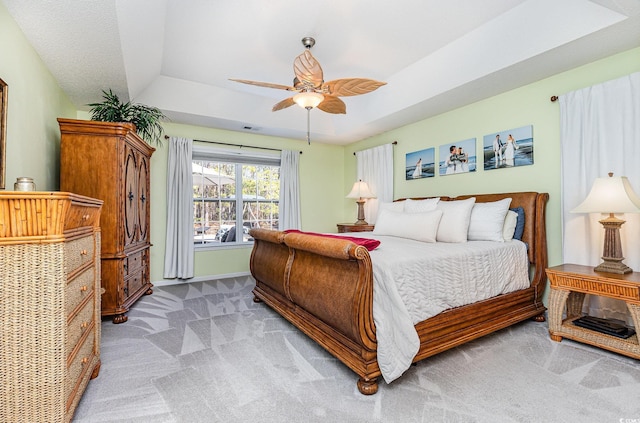 bedroom with vaulted ceiling, ceiling fan, light colored carpet, and a raised ceiling