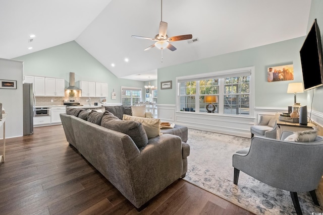 living room with dark wood-type flooring, ceiling fan with notable chandelier, and high vaulted ceiling