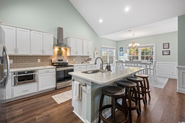 kitchen featuring appliances with stainless steel finishes, decorative light fixtures, wall chimney exhaust hood, white cabinets, and sink