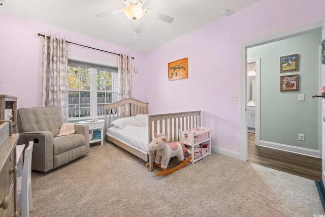 carpeted bedroom featuring ceiling fan, a nursery area, and ensuite bathroom