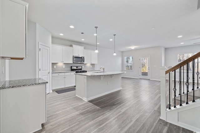 kitchen featuring appliances with stainless steel finishes, hanging light fixtures, light hardwood / wood-style floors, white cabinets, and a center island with sink