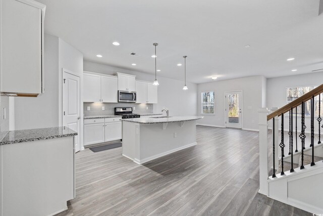 kitchen with a center island with sink, light stone countertops, white cabinets, and appliances with stainless steel finishes