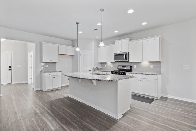 kitchen with white cabinetry, appliances with stainless steel finishes, a center island with sink, and light stone counters