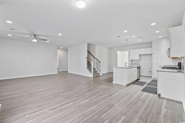 kitchen with white cabinetry, decorative light fixtures, a center island with sink, light hardwood / wood-style flooring, and stainless steel dishwasher