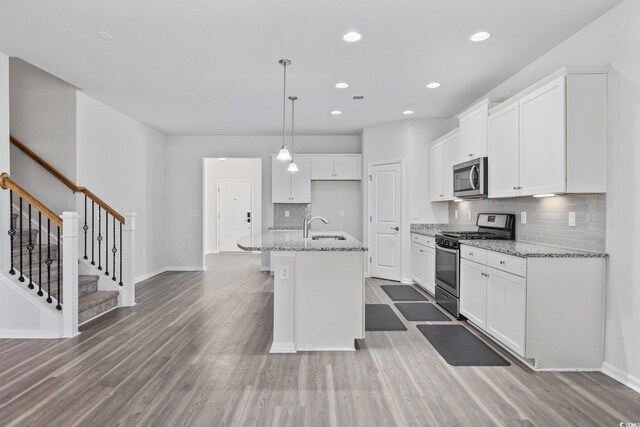 kitchen featuring light stone counters, decorative light fixtures, a center island with sink, stainless steel appliances, and white cabinets