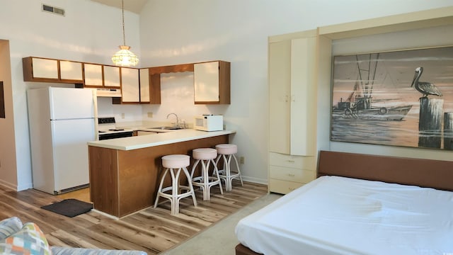 kitchen featuring kitchen peninsula, white appliances, light wood-type flooring, hanging light fixtures, and sink