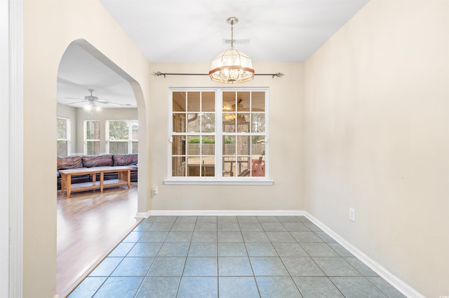 unfurnished dining area with ceiling fan with notable chandelier and tile patterned flooring