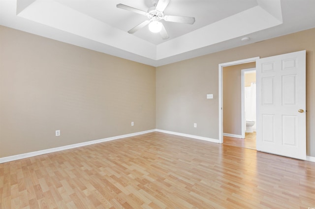 empty room with light hardwood / wood-style floors, a tray ceiling, and ceiling fan