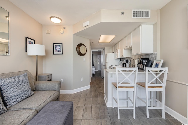 kitchen with kitchen peninsula, decorative backsplash, a kitchen bar, white appliances, and white cabinetry