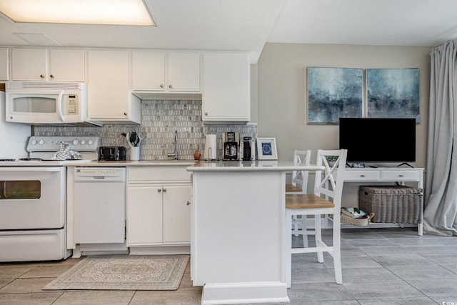 kitchen with a kitchen bar, decorative backsplash, sink, white appliances, and white cabinetry