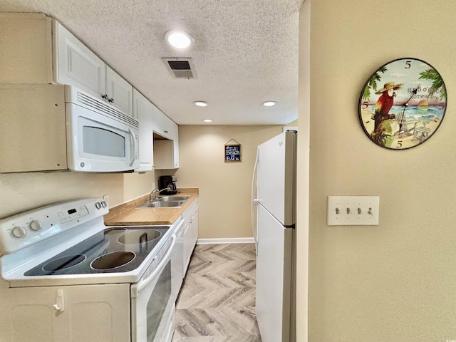 kitchen with light parquet flooring, sink, white appliances, a textured ceiling, and white cabinets