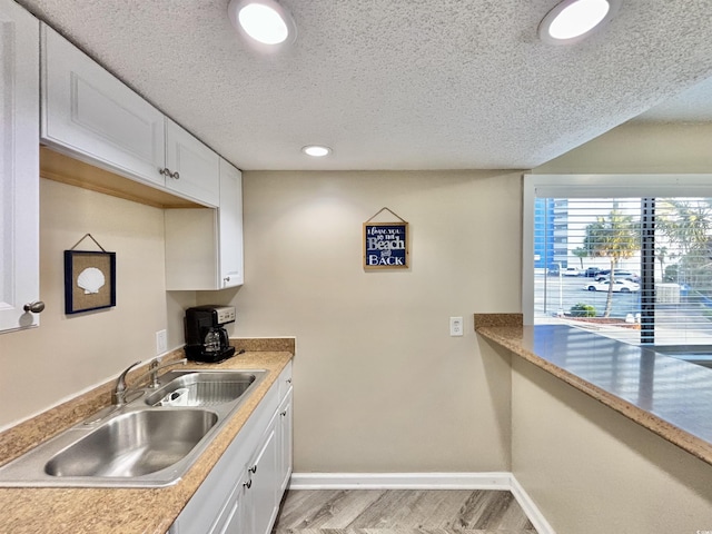 kitchen with sink, white cabinetry, light hardwood / wood-style flooring, and a textured ceiling