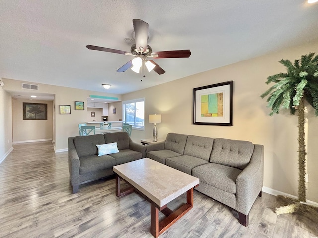 living room featuring ceiling fan, a textured ceiling, and hardwood / wood-style flooring