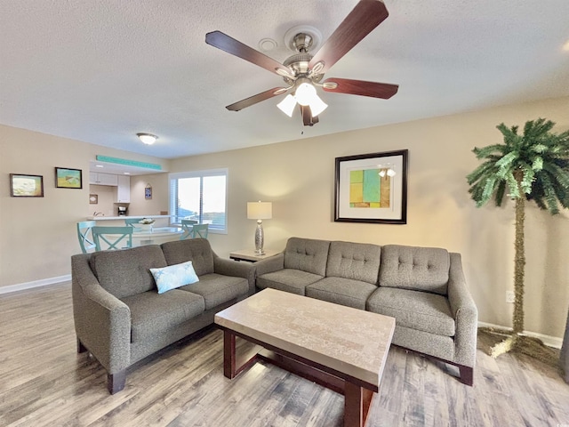 living room featuring light wood-type flooring, ceiling fan, and a textured ceiling