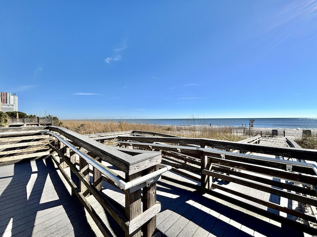 wooden terrace featuring a beach view and a water view