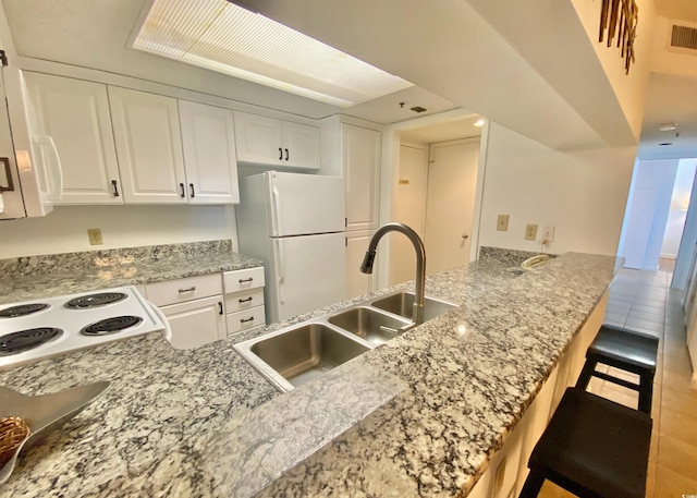 kitchen with a breakfast bar, kitchen peninsula, sink, white appliances, and white cabinetry