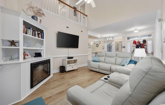 living room featuring ceiling fan with notable chandelier, ornamental molding, a high ceiling, and light wood-type flooring