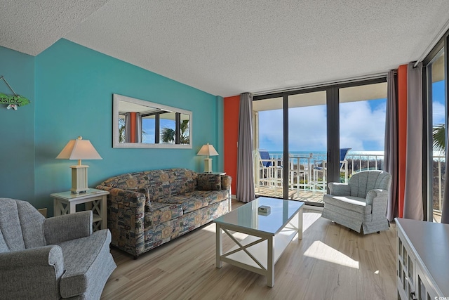 living room featuring a water view, a wall of windows, light hardwood / wood-style flooring, and a textured ceiling