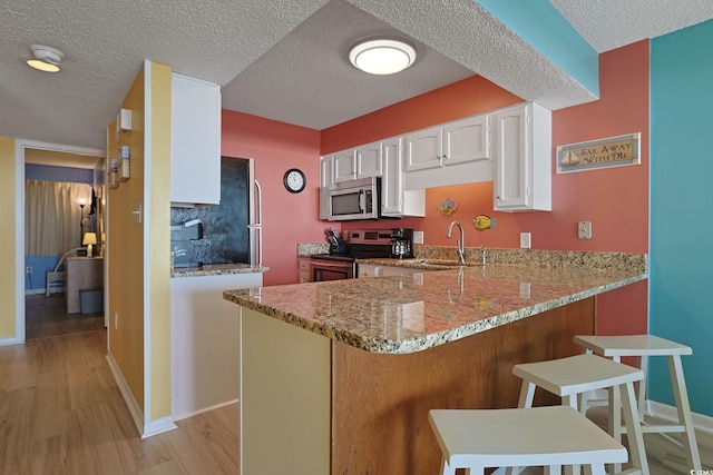 kitchen featuring a kitchen bar, light wood-type flooring, appliances with stainless steel finishes, kitchen peninsula, and white cabinets