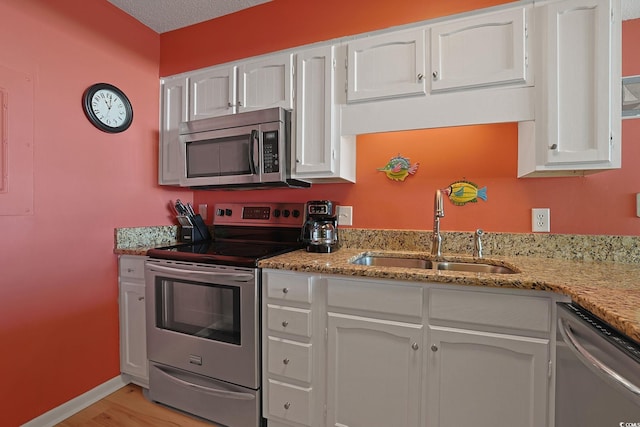 kitchen with sink, white cabinets, stainless steel appliances, light stone countertops, and light wood-type flooring