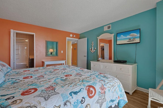 bedroom featuring ensuite bathroom, a textured ceiling, and light hardwood / wood-style floors