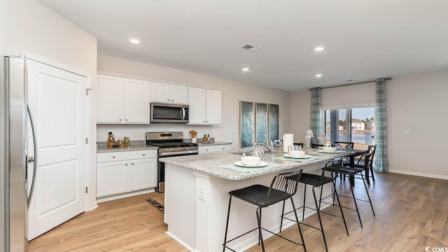 kitchen featuring light stone countertops, appliances with stainless steel finishes, white cabinets, and an island with sink