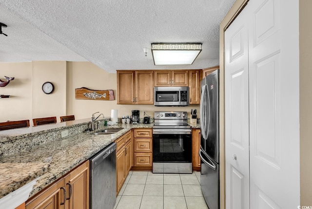 kitchen with a breakfast bar area, stainless steel appliances, light tile patterned flooring, light stone counters, and sink