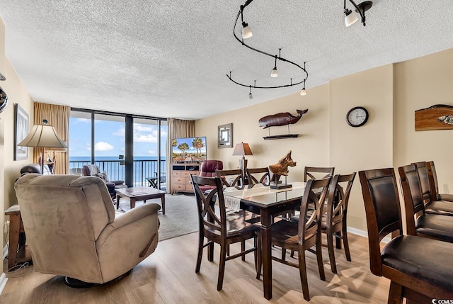 dining space with a textured ceiling, track lighting, floor to ceiling windows, and light hardwood / wood-style flooring