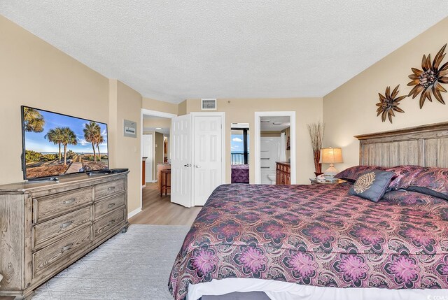 bedroom with ensuite bathroom, a textured ceiling, and light hardwood / wood-style flooring