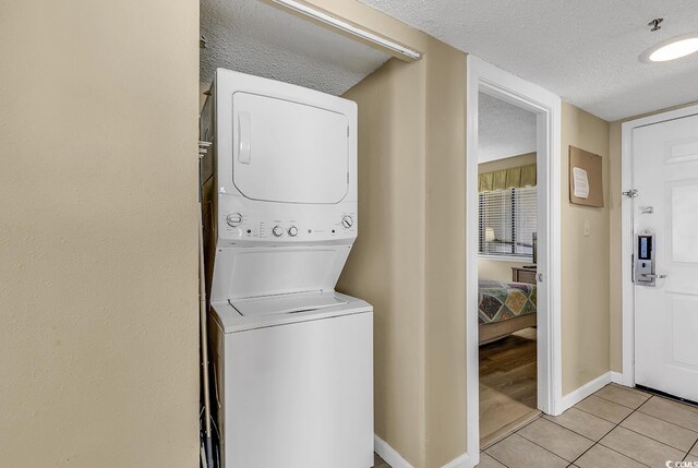 clothes washing area featuring stacked washing maching and dryer, light tile patterned floors, and a textured ceiling