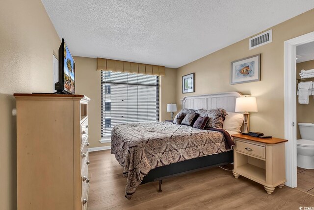 bedroom featuring ensuite bath, a textured ceiling, light wood-type flooring, and multiple windows