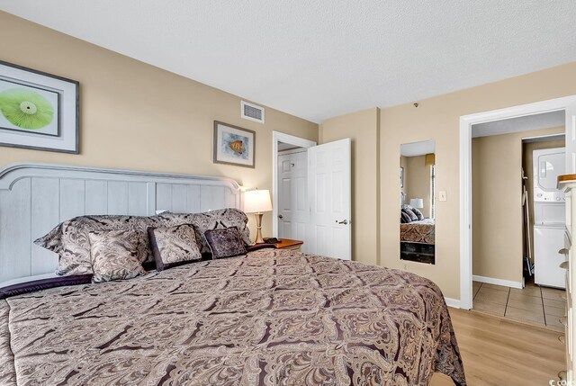 bedroom with light wood-type flooring, a textured ceiling, and washer / dryer