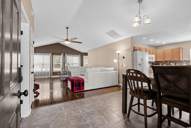 dining area featuring ceiling fan with notable chandelier and vaulted ceiling