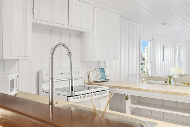 kitchen with white cabinetry, white appliances, wood walls, and crown molding