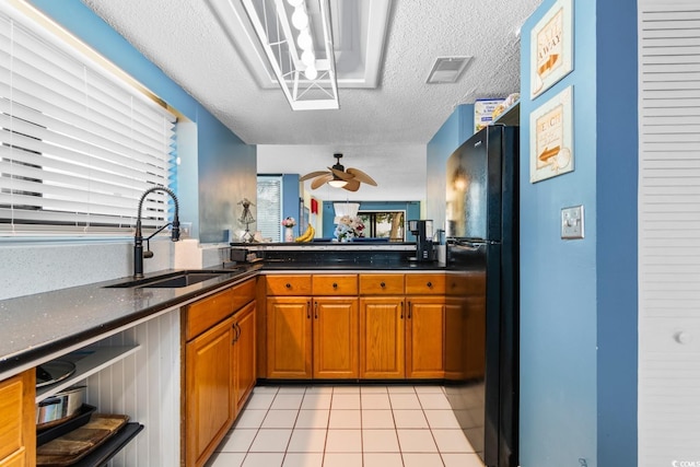 kitchen with a textured ceiling, sink, black fridge, ceiling fan, and light tile patterned floors