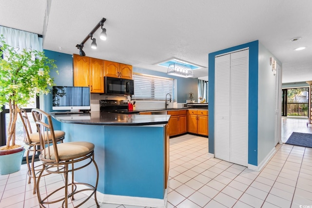 kitchen with light tile patterned floors, kitchen peninsula, electric stove, a breakfast bar, and sink