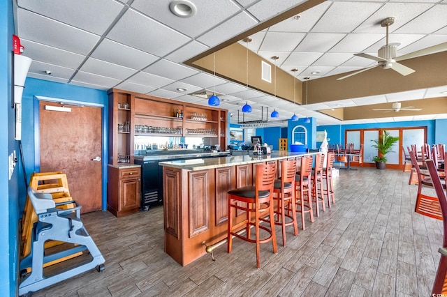 kitchen with ceiling fan, a kitchen bar, kitchen peninsula, a paneled ceiling, and light stone countertops