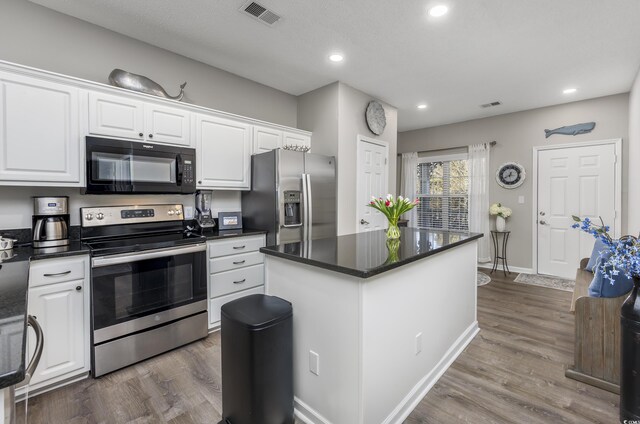 kitchen with appliances with stainless steel finishes, wood-type flooring, white cabinetry, and a center island