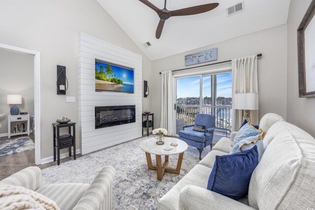 living room featuring ceiling fan, wood-type flooring, high vaulted ceiling, and a large fireplace